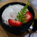 Homemade ice cream in a bowl with strawberries and a fern