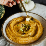 Roasted butternut squash soup with herbs in a bowl, stirred with a gold spoon