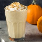 pumpkin spice milkshake with whipped cream with cinnamon sticks and little pumpkins in the background